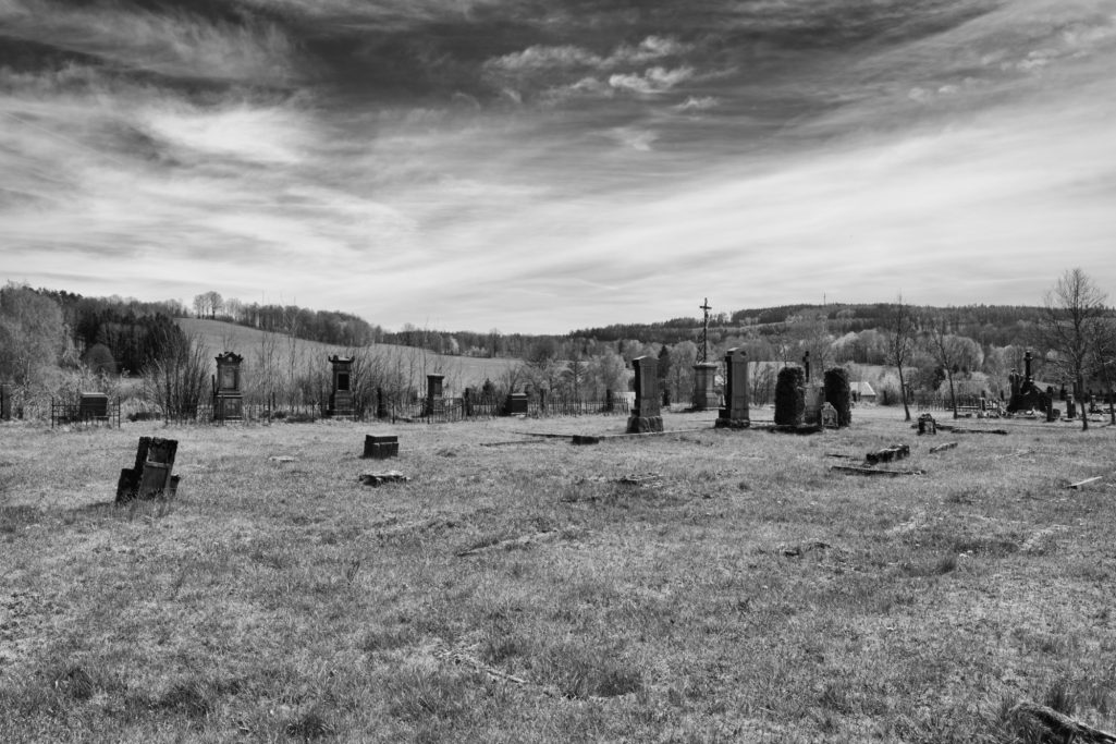 Alter deutscher Friedhof bei Lobendava Graues Feld mit mehreren Steinen und einer bewölkten Himmel im Hintergrund.